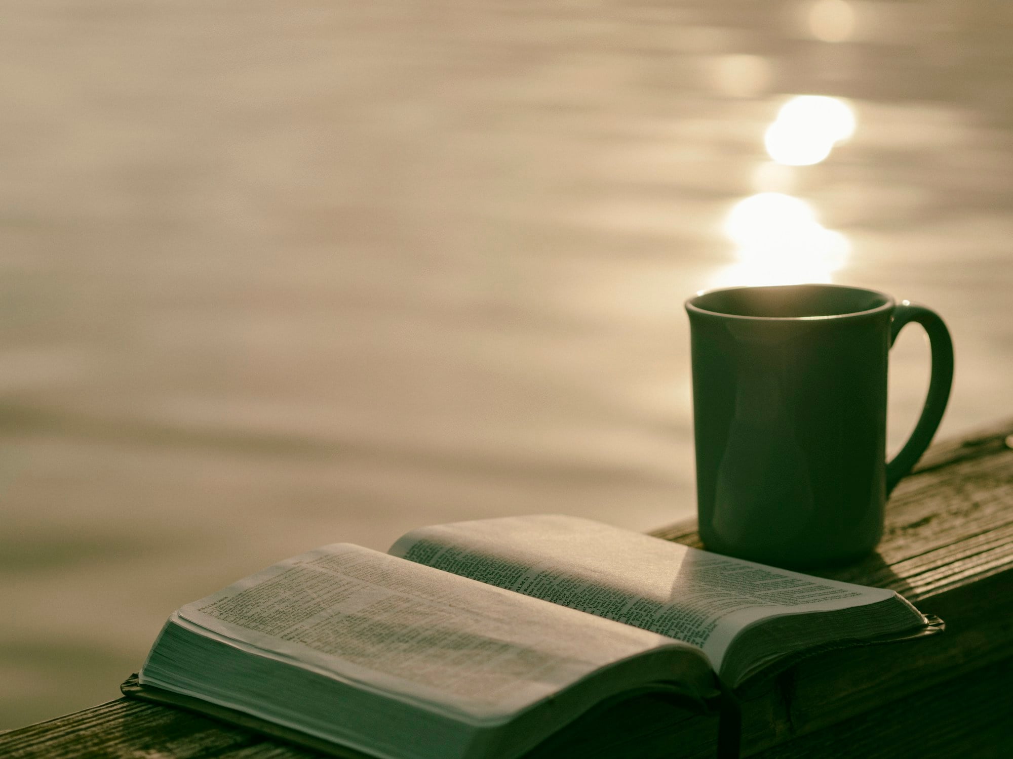 A green mug beside an open book in soft morning light