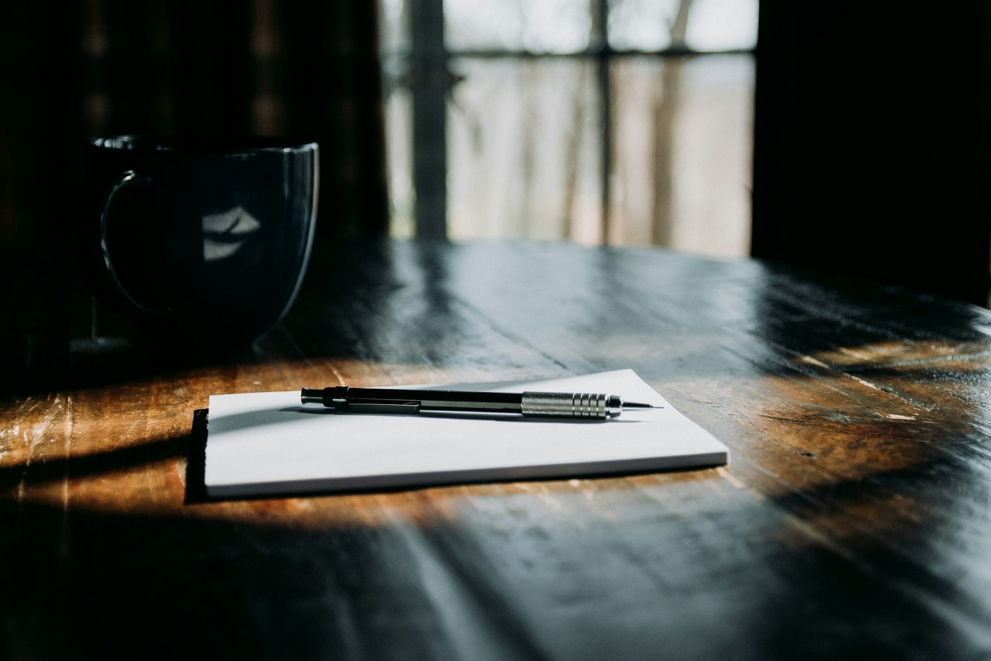 A notebook and pen on a sunlit wooden table, ready for a monthly retreat guide