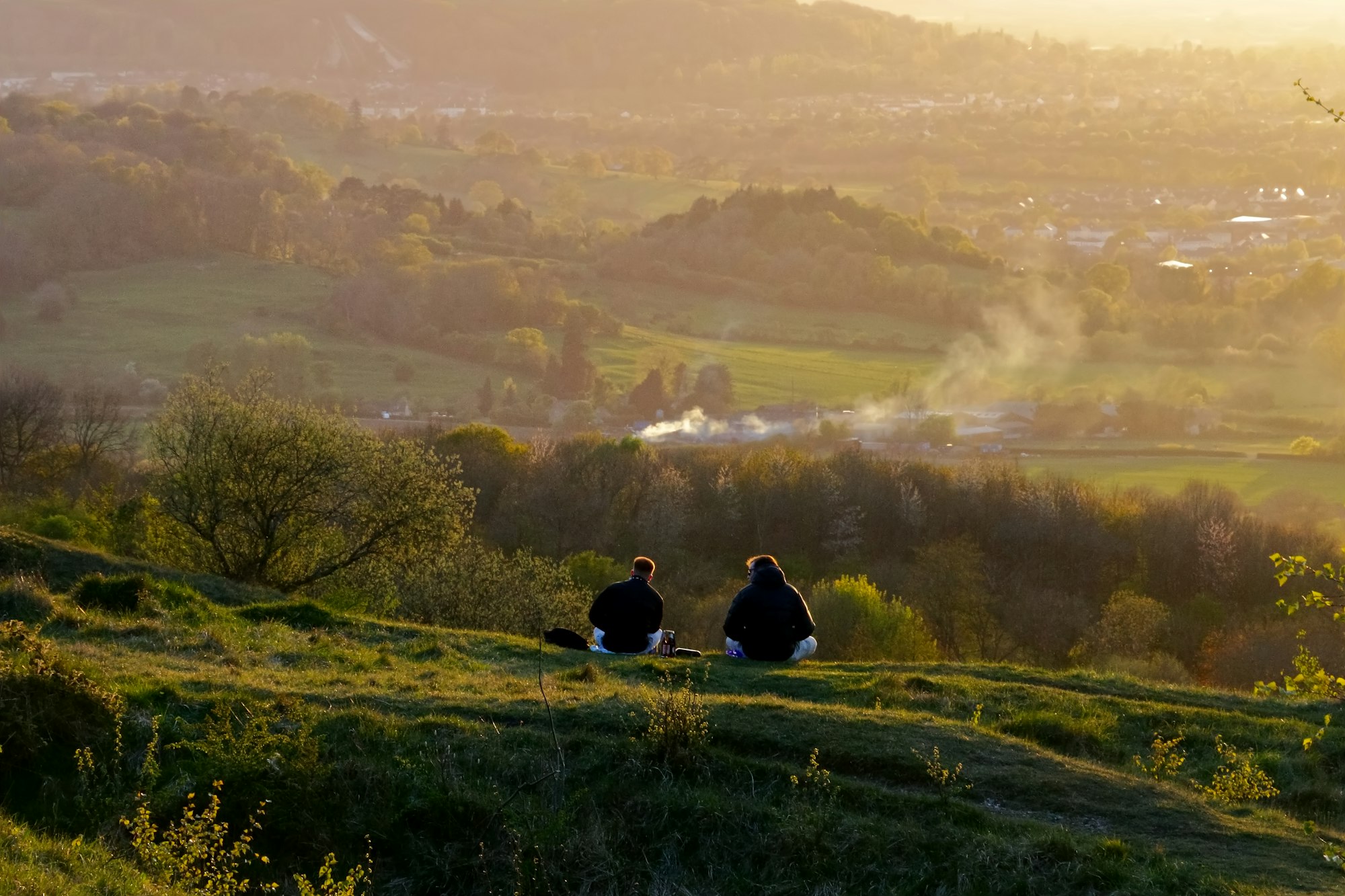 Two people sitting on a hillside in golden evening light, retreating together