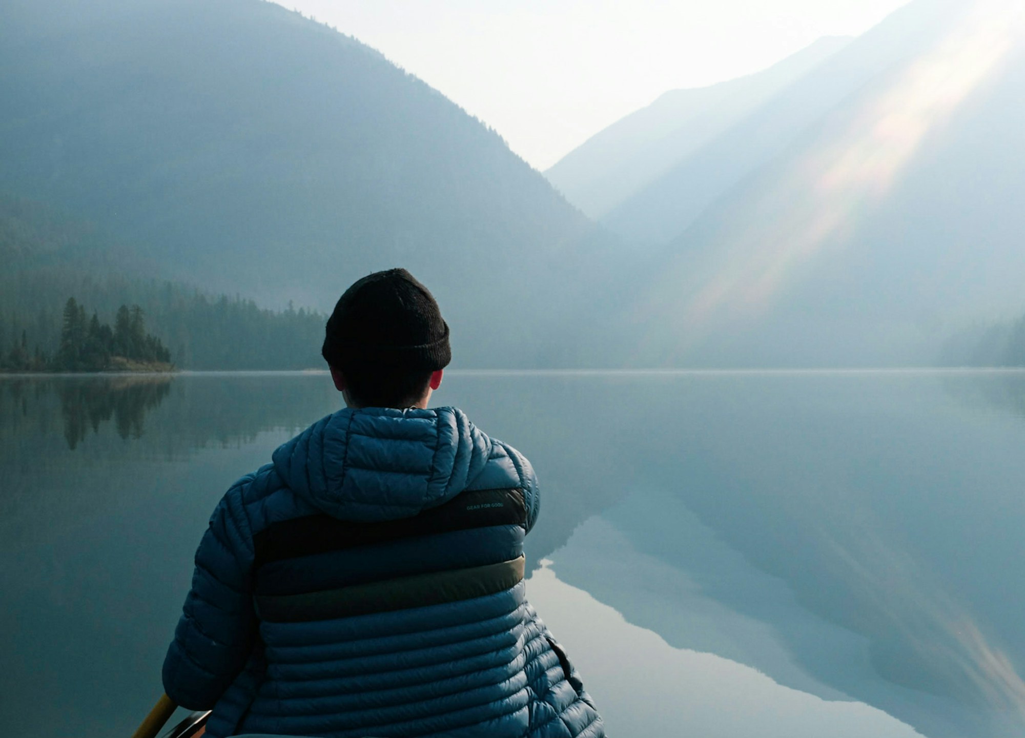 A person sitting by a still mountain lake in the early morning