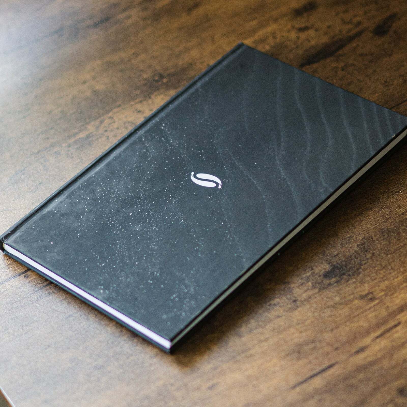 The black cover of the Soul Care Journal on a wooden table, a guided journal gift for staff